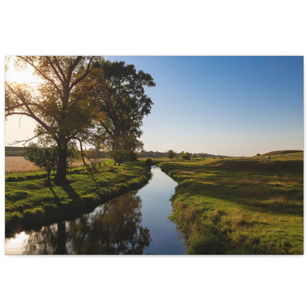 A creek winding through the prairie pasture reflecting the deep blue sky with sunlight shining on the green grass.