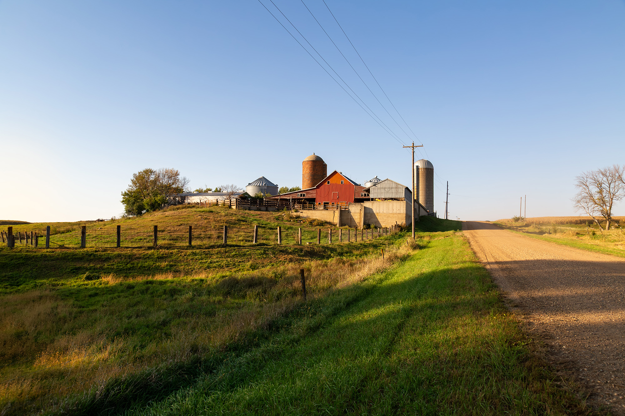 A small farm at the top of the hill along a gravel road with rustic red barn and a silo.